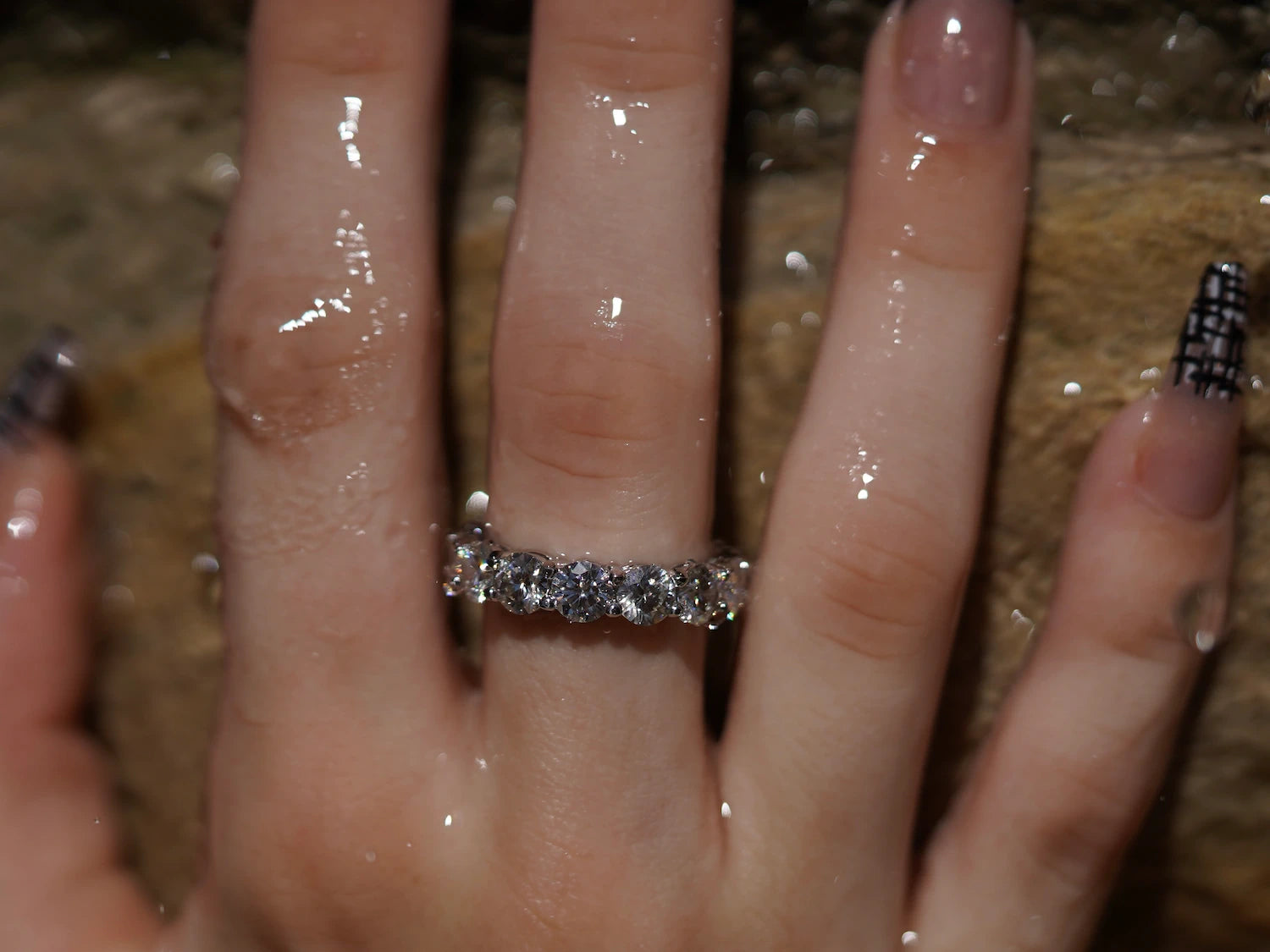 Moissanit Eternity-Ring mit 5 mm Steinen vor Sandsteinwand – kraftvoller Moissanite Ring aus Sterling Silber mit Weißgold, durchgehendes Funkeln und luxuriöse Präsenz.
