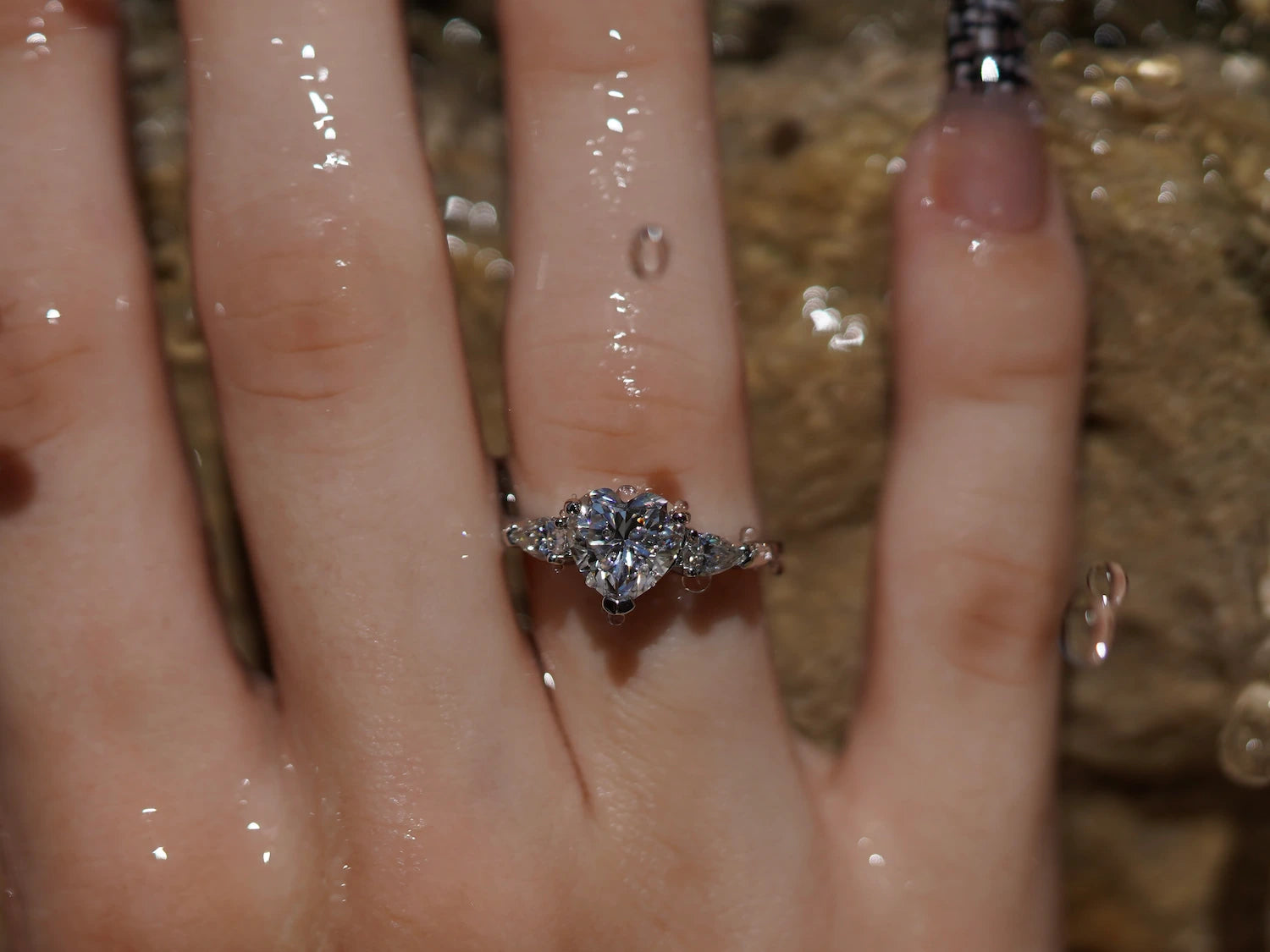 Moissanite Ring mit Herzschliff und tropfenförmigen Nebensteinen vor Wasser, eleganter Moissanite Schmuck aus Sterling Silber mit Weißgold, ausdrucksstarker Moissanite Ring mit emotionalem Design und funkelnder Tiefe.