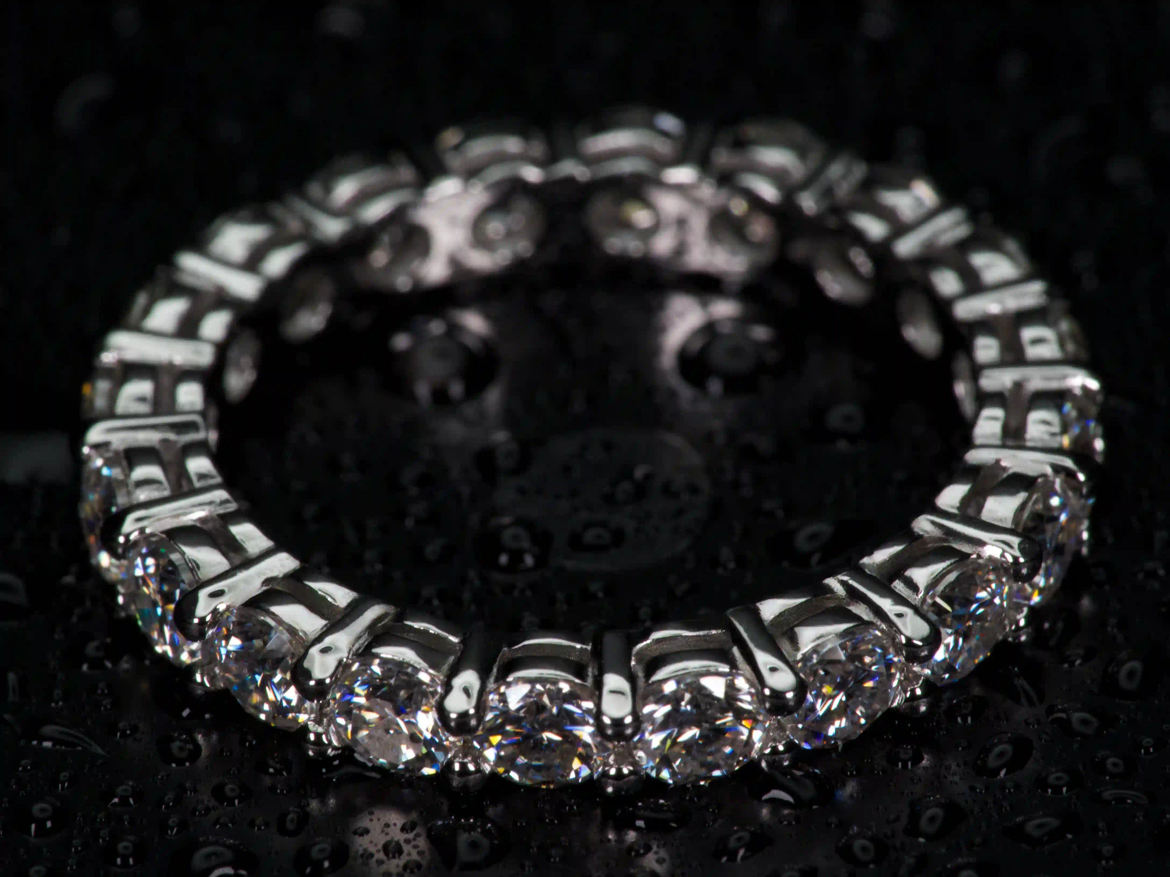 Echte Makroaufnahme eines 3mm Moissanite Eternity Rings aus 925 Silber & Weißgold im echten Licht. Rundum gefasste Moissanite mit stärkerem Funkeln als Diamanten erzeugen intensive Lichtreflexe, sichtbares Feuer und auffällige Brillanz im Alltag. Echte Fotos mit präziser Krappenfassung und hochwertiger Verarbeitung.