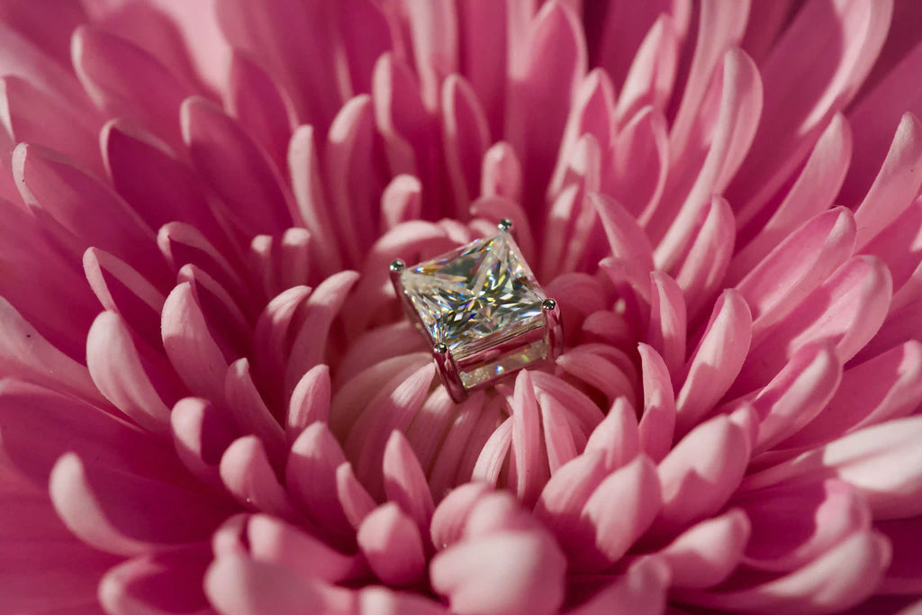 Echte Fotos von stark funkelnden Princess Cut Moissanite Ohrsteckern mit 4 Zinken auf einer rosa Blüte im echten Licht fotografiert – stärkeres Funkeln als Diamant mit intensivem Lichtspiel.