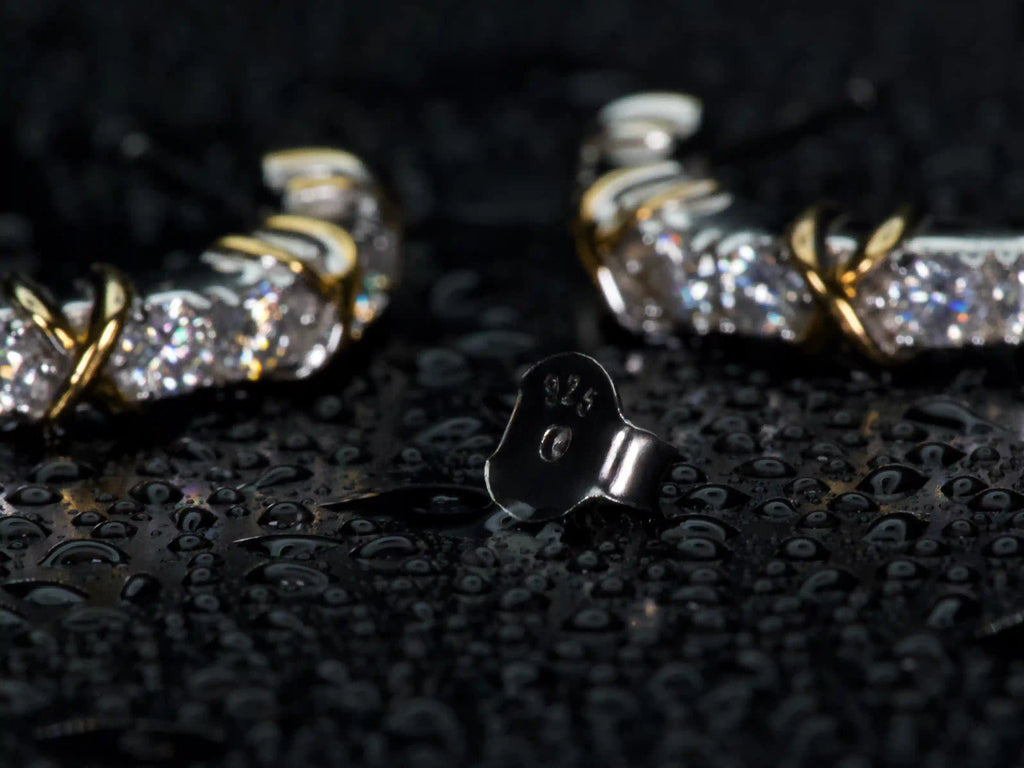 Echte Fotos zeigen 925 Silber Stempel und Butterflyverschluss der Moissanit Creolen im Fokus, im Hintergrund funkeln 3mm Steine mit 1ct pro Ohrring stärker als Diamant im echten Licht, Weißgold und Gelbgold Veredelung sichtbar