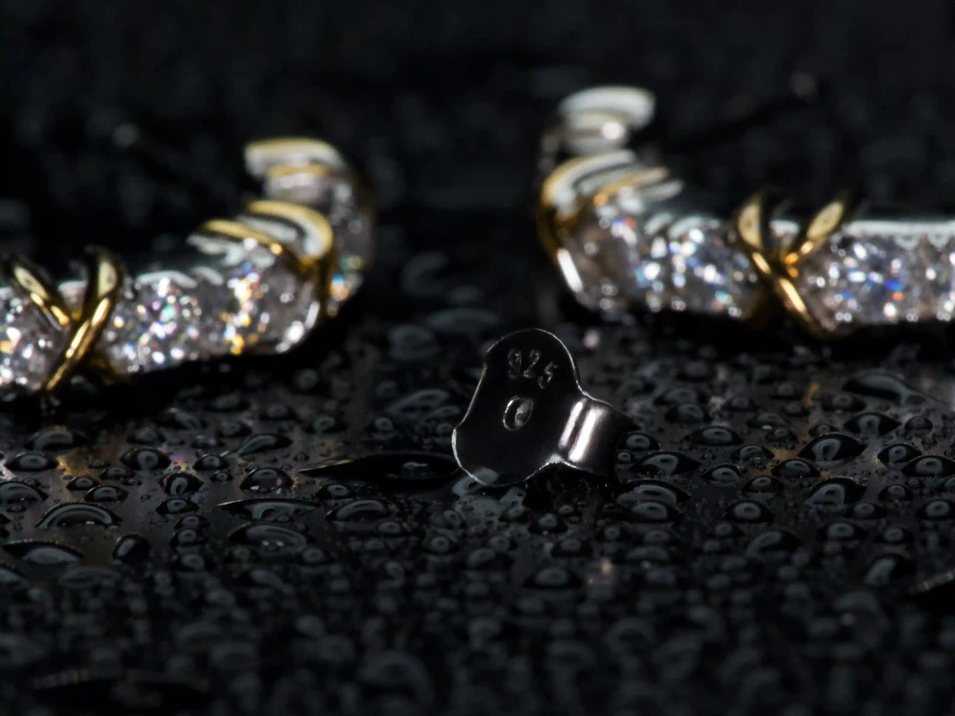 Echte Fotos zeigen 925 Silber Stempel und Butterflyverschluss der Moissanit Creolen im Fokus, im Hintergrund funkeln 3mm Steine mit 1ct pro Ohrring stärker als Diamant im echten Licht, Weißgold und Gelbgold Veredelung sichtbar