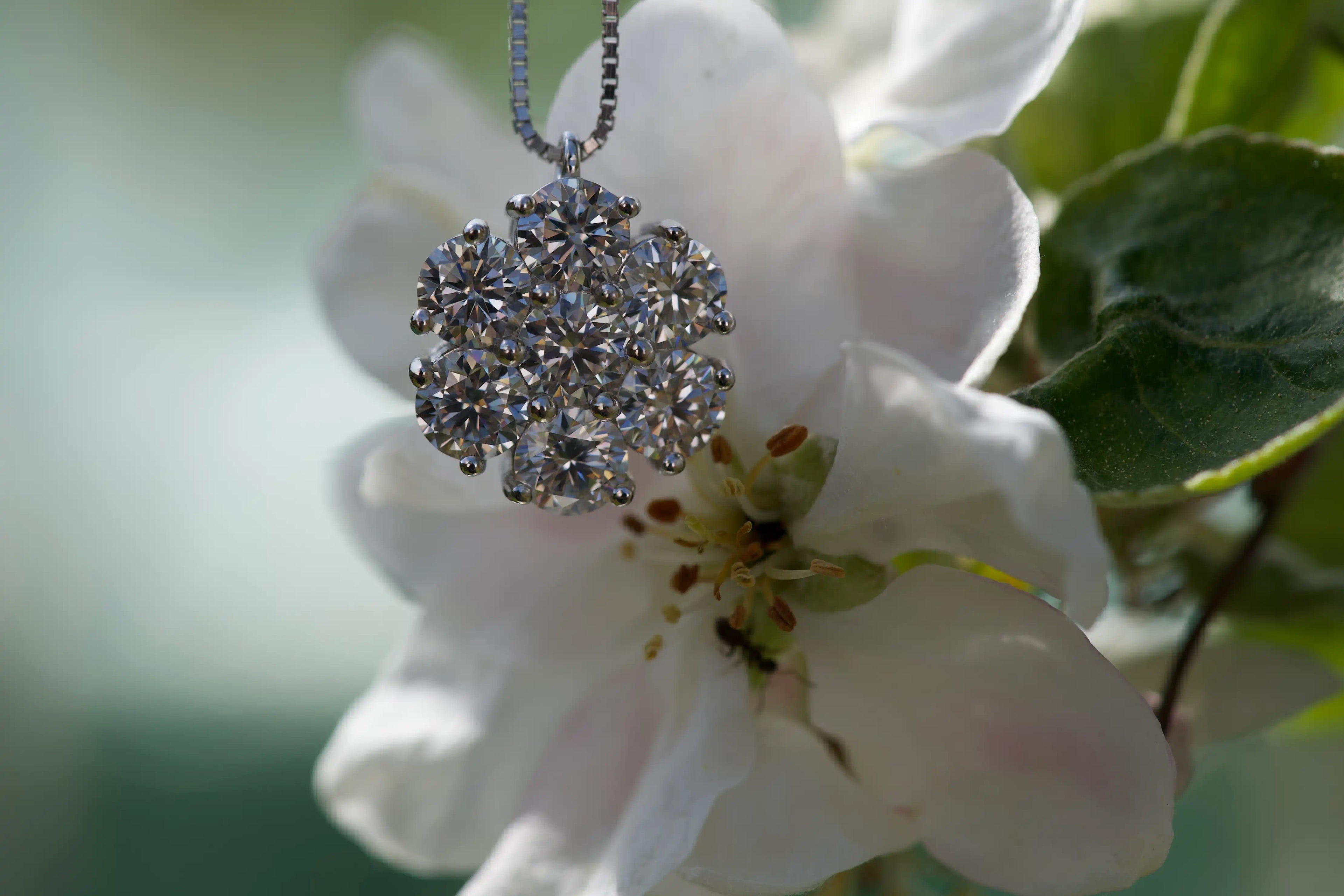 Moissanit Cluster Kette zwischen weißer Blüte im echten Licht fotografiert. Die starke Brillanz der Moissanite erinnert an Diamanten und erzeugt intensive Lichtreflexe in natürlicher Umgebung.