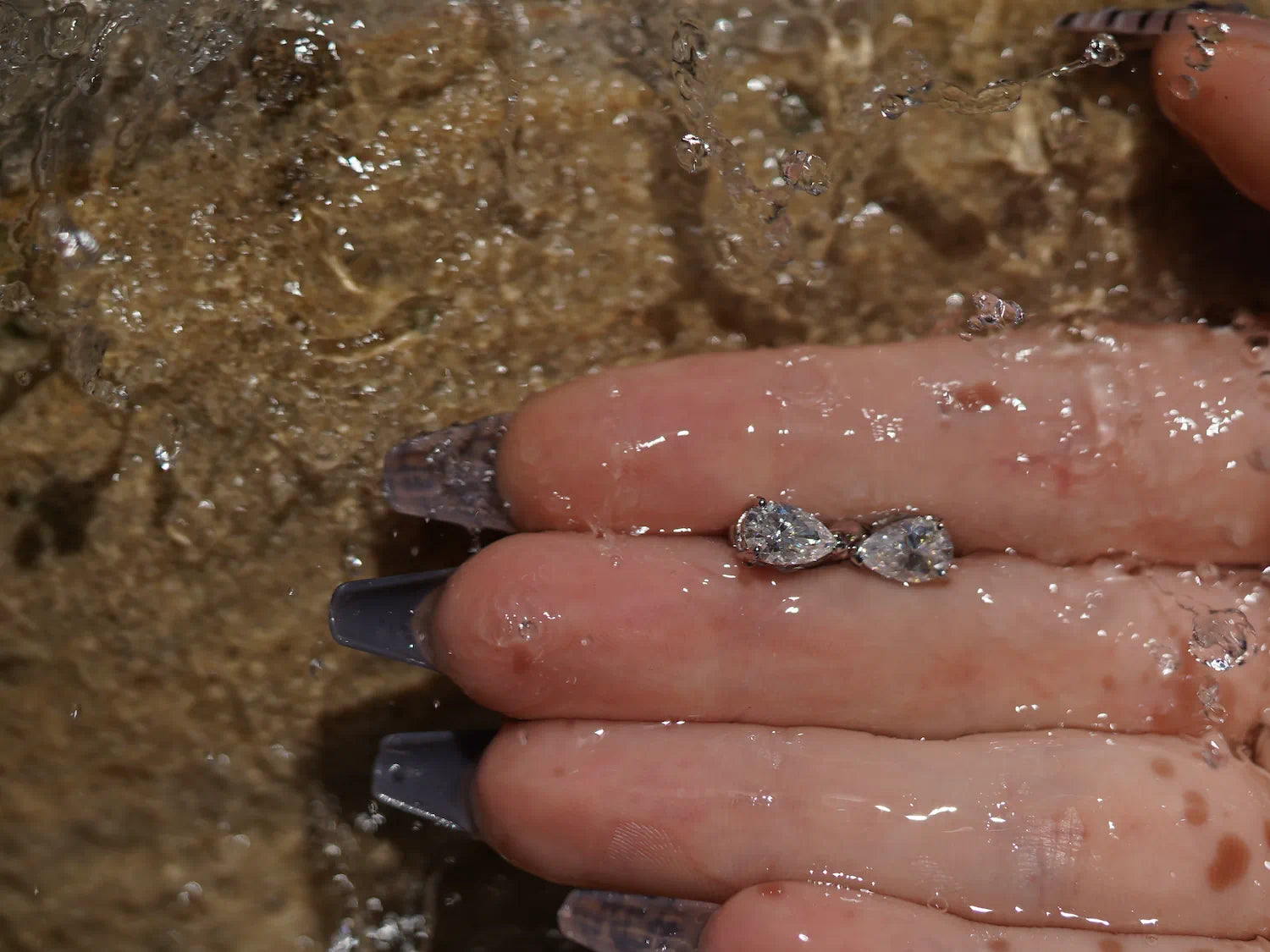 Tropfenförmige Moissanite Ohrstecker vor Sandsteinwand – Moissanite Schmuck aus Sterling Silber mit Weißgold, eleganter Tropfenschliff und feine Lichtreflexe.