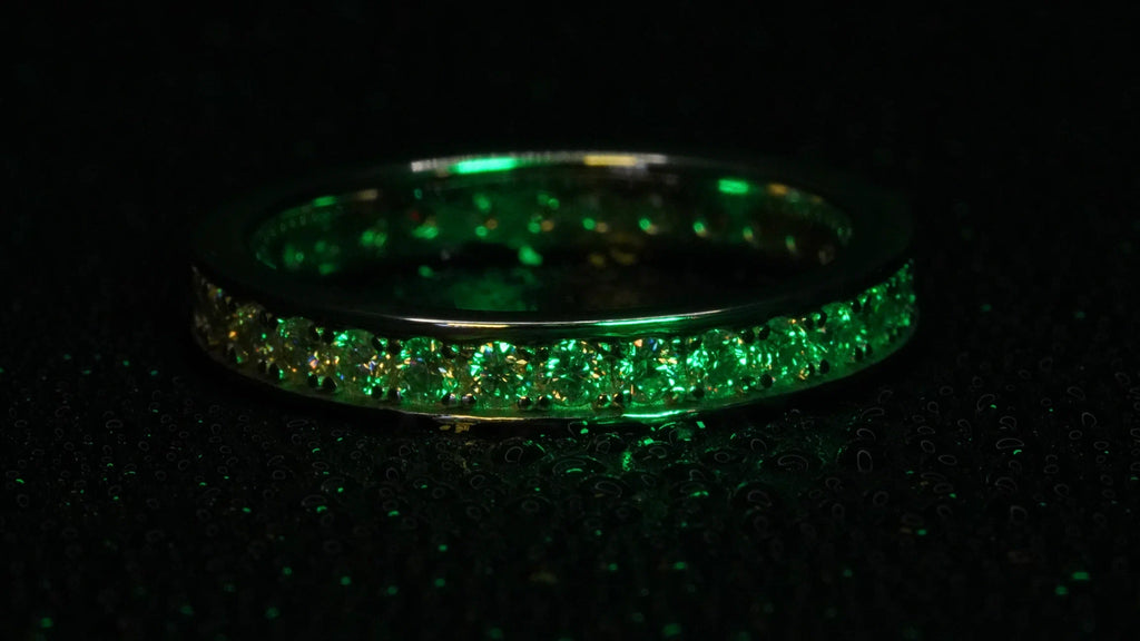 Moissanite Eternity Ring mit Rand funkelt in grünem Licht. Gefasst in Silber