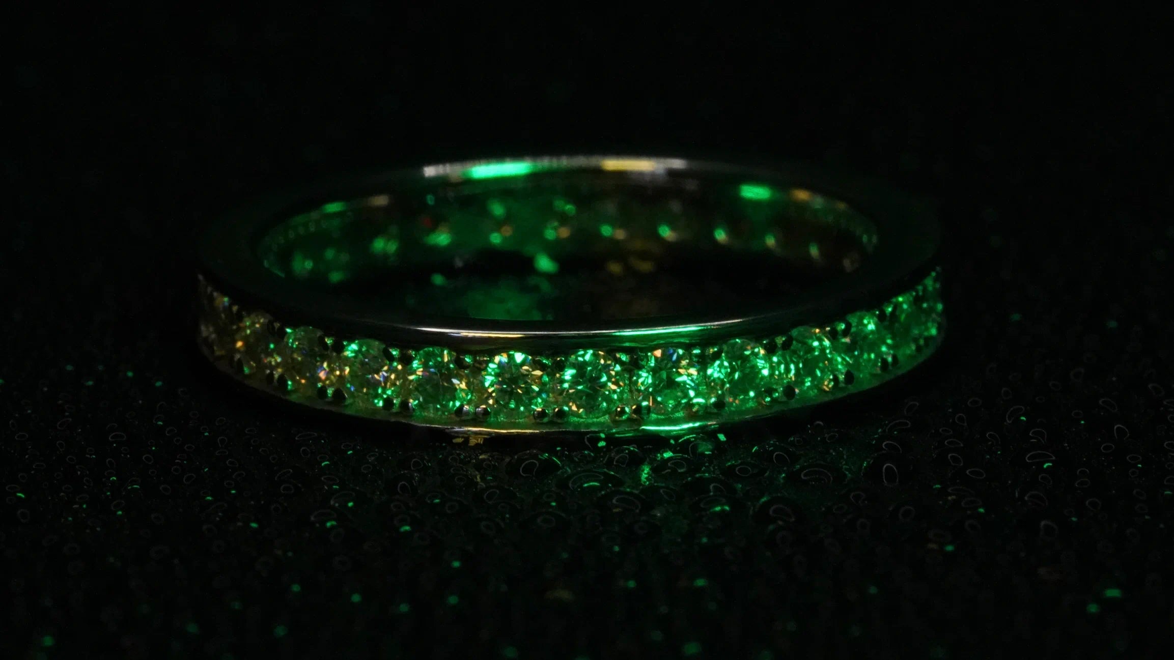Moissanite Eternity Ring mit Rand funkelt in grünem Licht. Gefasst in Silber