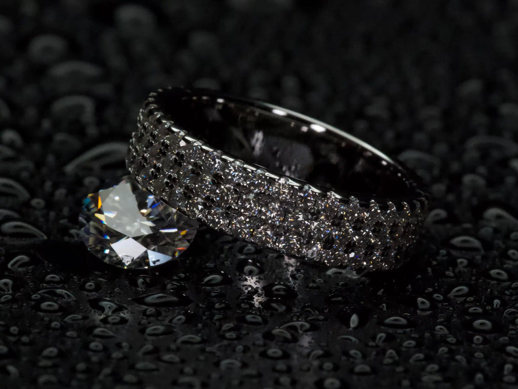 Moissanite Eternity Ring mit drei Reihen 1 mm Steinen von oben fotografiert, neben einem 2 ct Moissanite Stein, 925 Silber mit Weißgold Veredelung, echte Fotos ohne Glanzfilter