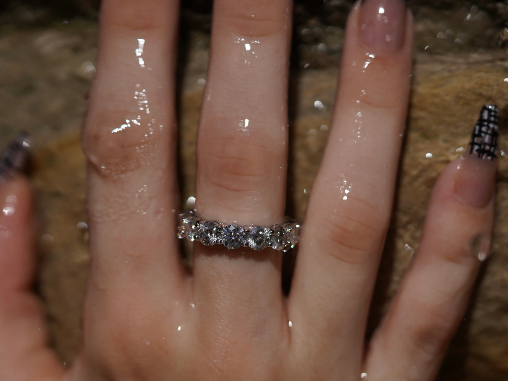 Moissanit Eternity-Ring mit 5 mm Steinen vor Sandsteinwand – kraftvoller Moissanite Ring aus Sterling Silber mit Weißgold, durchgehendes Funkeln und luxuriöse Präsenz.
