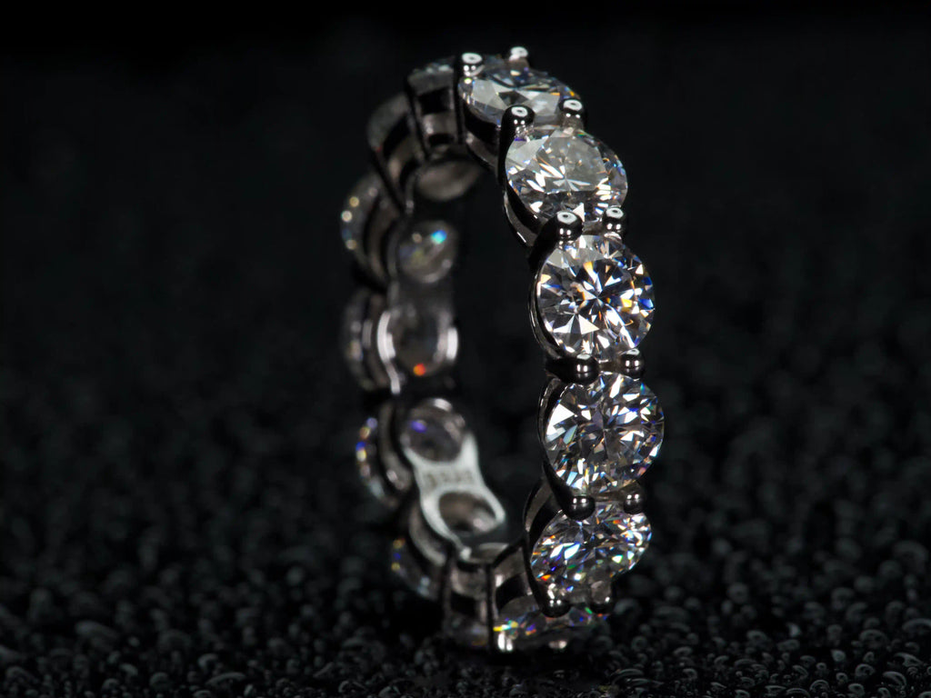 Moissanite Eternity Ring mit 5 mm Steinen stehend von der Seite fotografiert, sichtbare Fassung und Tiefe, starkes Funkeln bei echtem Licht, 925 Silber & 18K Weißgold, echte Fotos