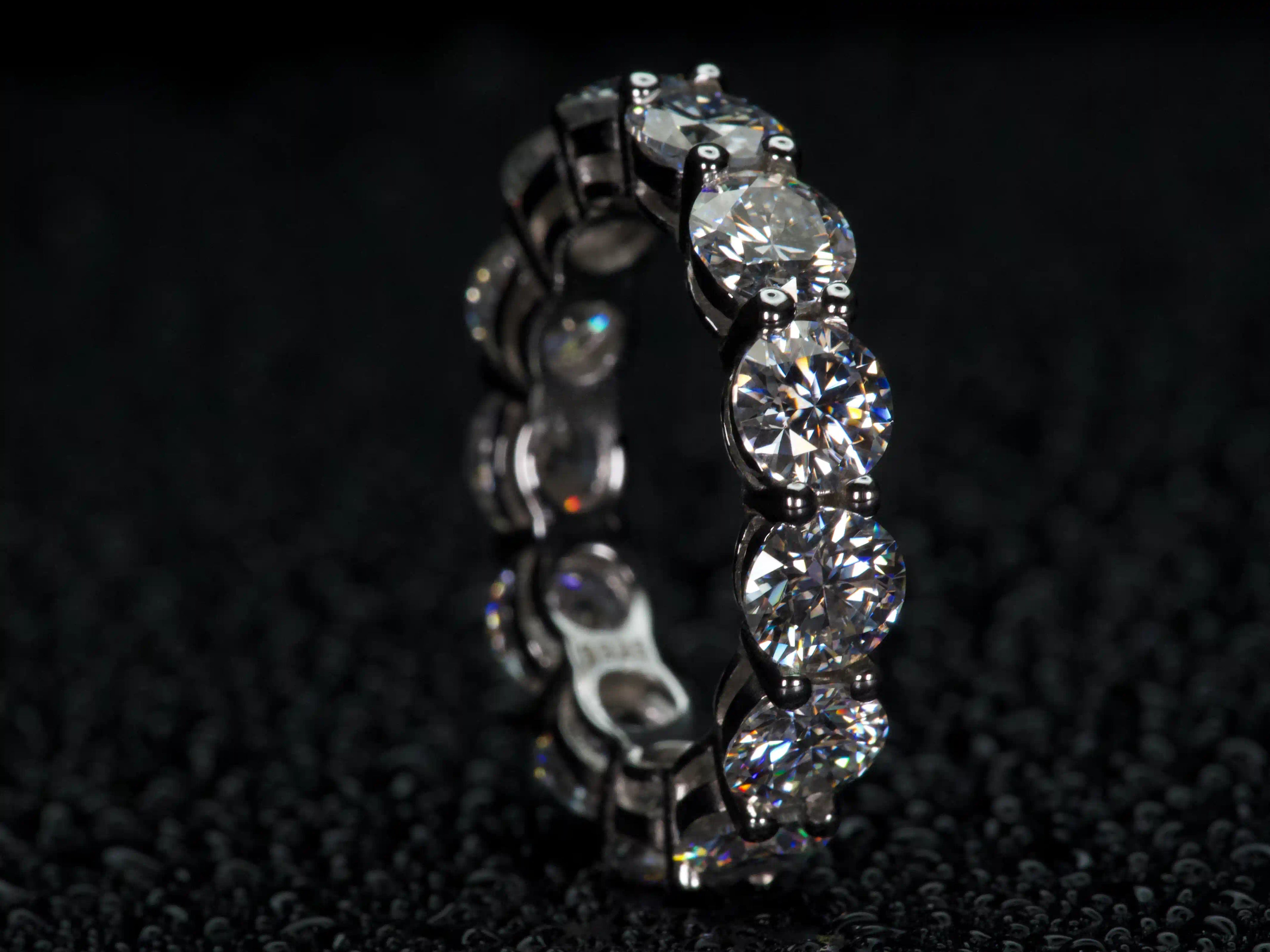 Moissanite Eternity Ring mit 5 mm Steinen stehend von der Seite fotografiert, sichtbare Fassung und Tiefe, starkes Funkeln bei echtem Licht, 925 Silber & 18K Weißgold, echte Fotos