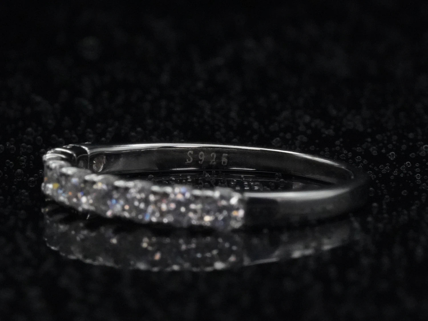 Makroaufnahme der Innenseite eines filigranen Halb-Eternity-Rings aus 925er Silber mit eingeprägtem „S925“-Stempel, dezent umrahmt von funkelnden Moissanite-Steinen, auf einem glänzenden schwarzen Untergrund