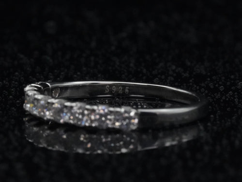 Makroaufnahme der Innenseite eines filigranen Halb-Eternity-Rings aus 925er Silber mit eingeprägtem „S925“-Stempel, dezent umrahmt von funkelnden Moissanite-Steinen, auf einem glänzenden schwarzen Untergrund