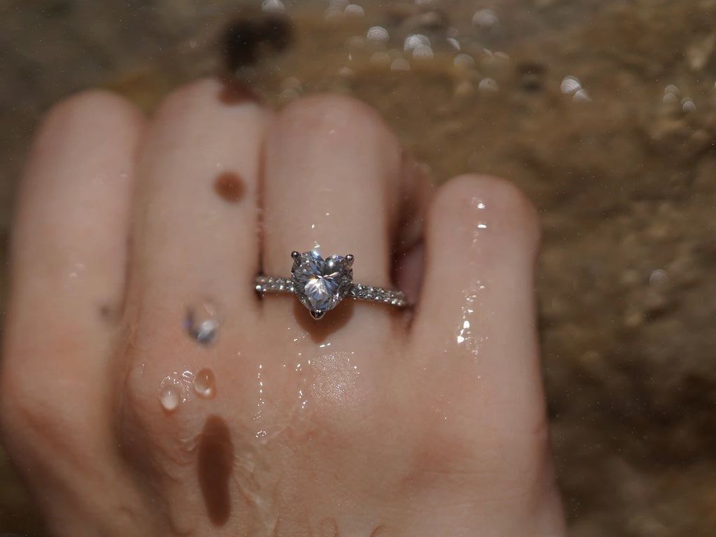 Moissanite Ring mit Herzschliff vor Sandsteinwand – ausdrucksstarker Moissanit Schmuck aus Sterling Silber mit Weißgold, emotionales Funkeln und modernes Design.