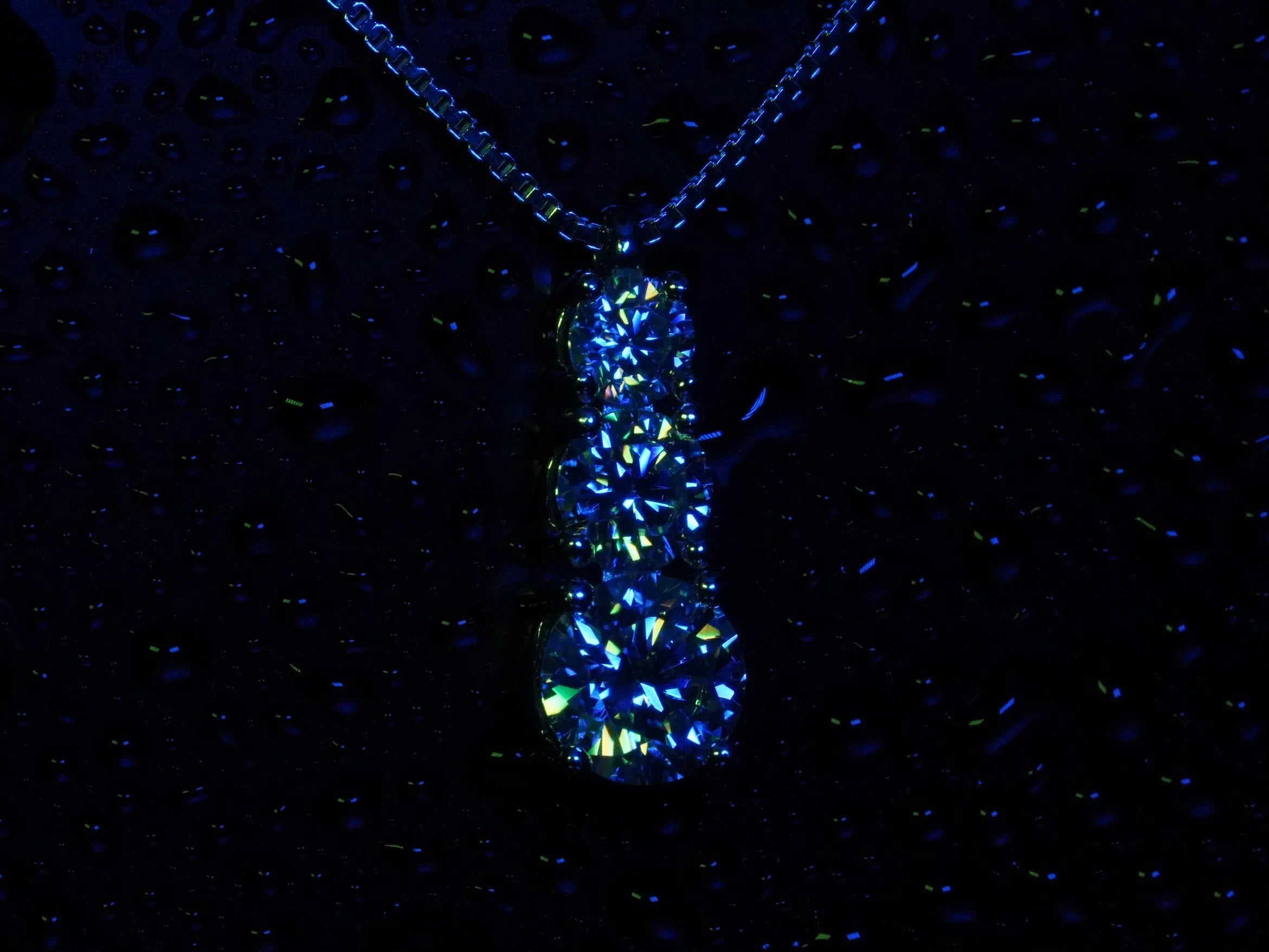 Funkelnde Moissanite Kette mit 3 Steinen in verschiedenen Größen in blau und grünem Licht 