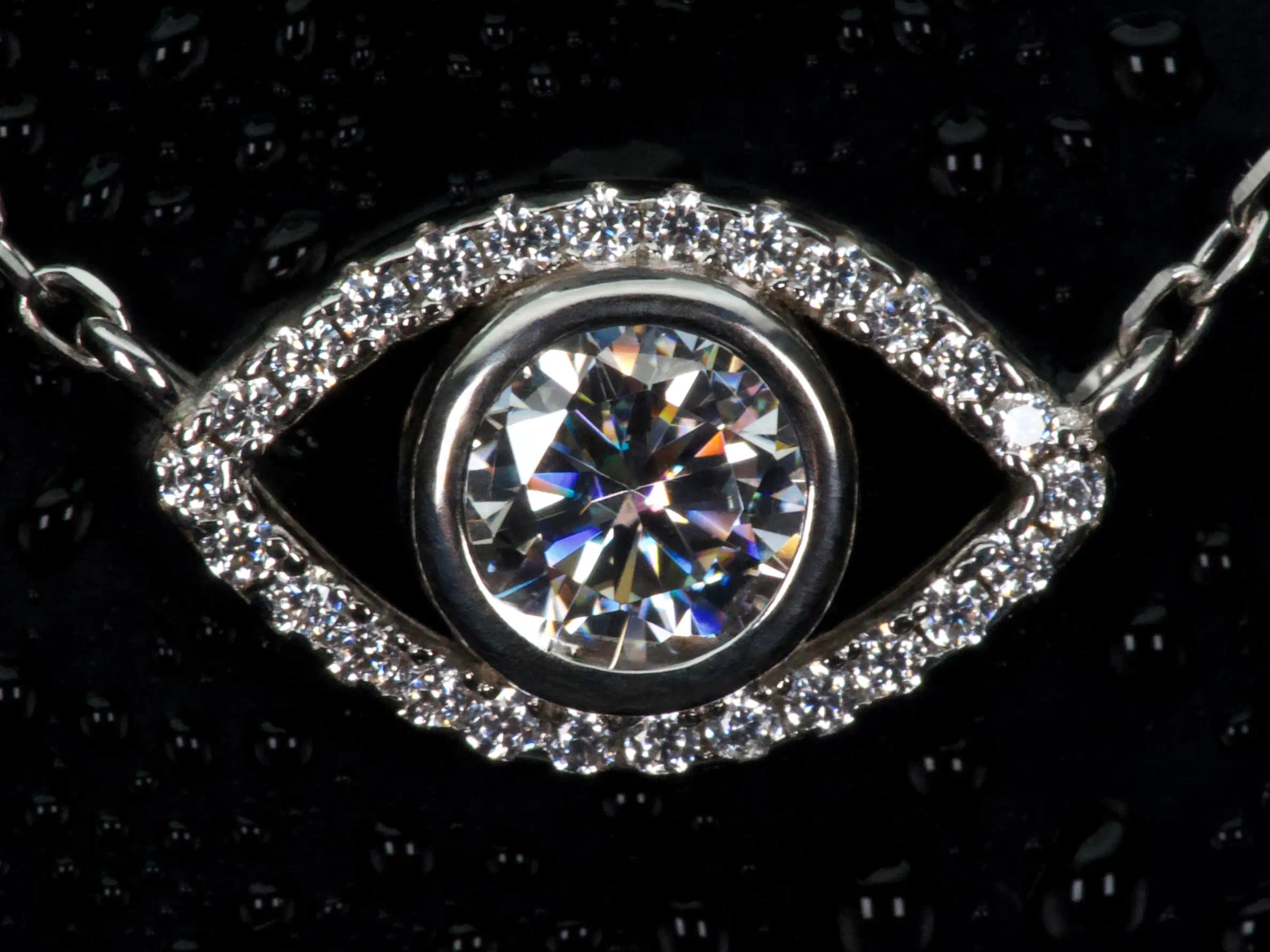 Echte Macro Aufnahme einer Moissanite Kette mit Auge Anhänger – zentraler Stein mit extremem Funkeln und Feuer im echten Licht, umgeben von feinem Halo, 925 Sterling Silber mit Weißgold Veredelung, auffälliger als Diamant im Vergleich