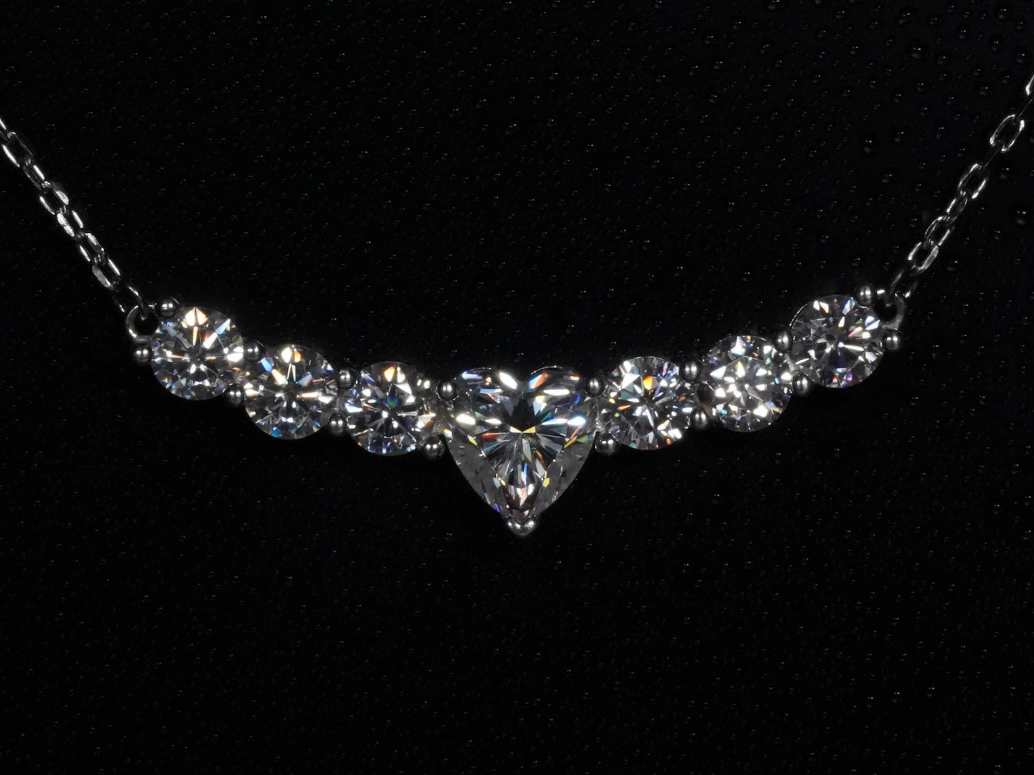 Moissanite-Kette mit Herzschliff – frontal fotografiert, zentraler Moissanite in Herzform mit sechs runden Steinen nebeneinander in gebogener Silberfassung