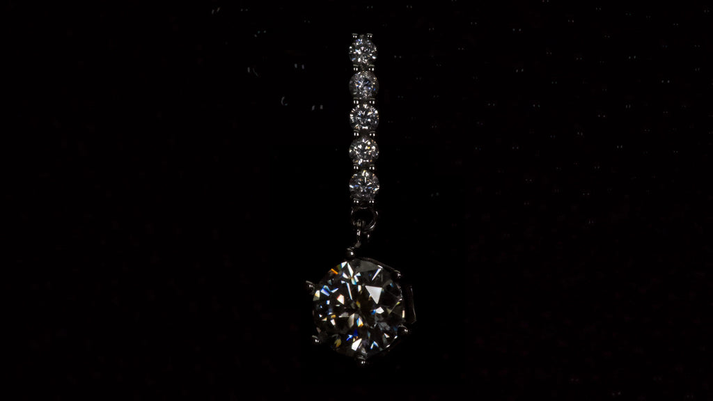 Detailwinkel eines Moissanite Ohrrings mit 1ct hängendem Brillantschliff Stein in dunkler Makroaufnahme aus 925 Silber mit Weißgold Veredelung
