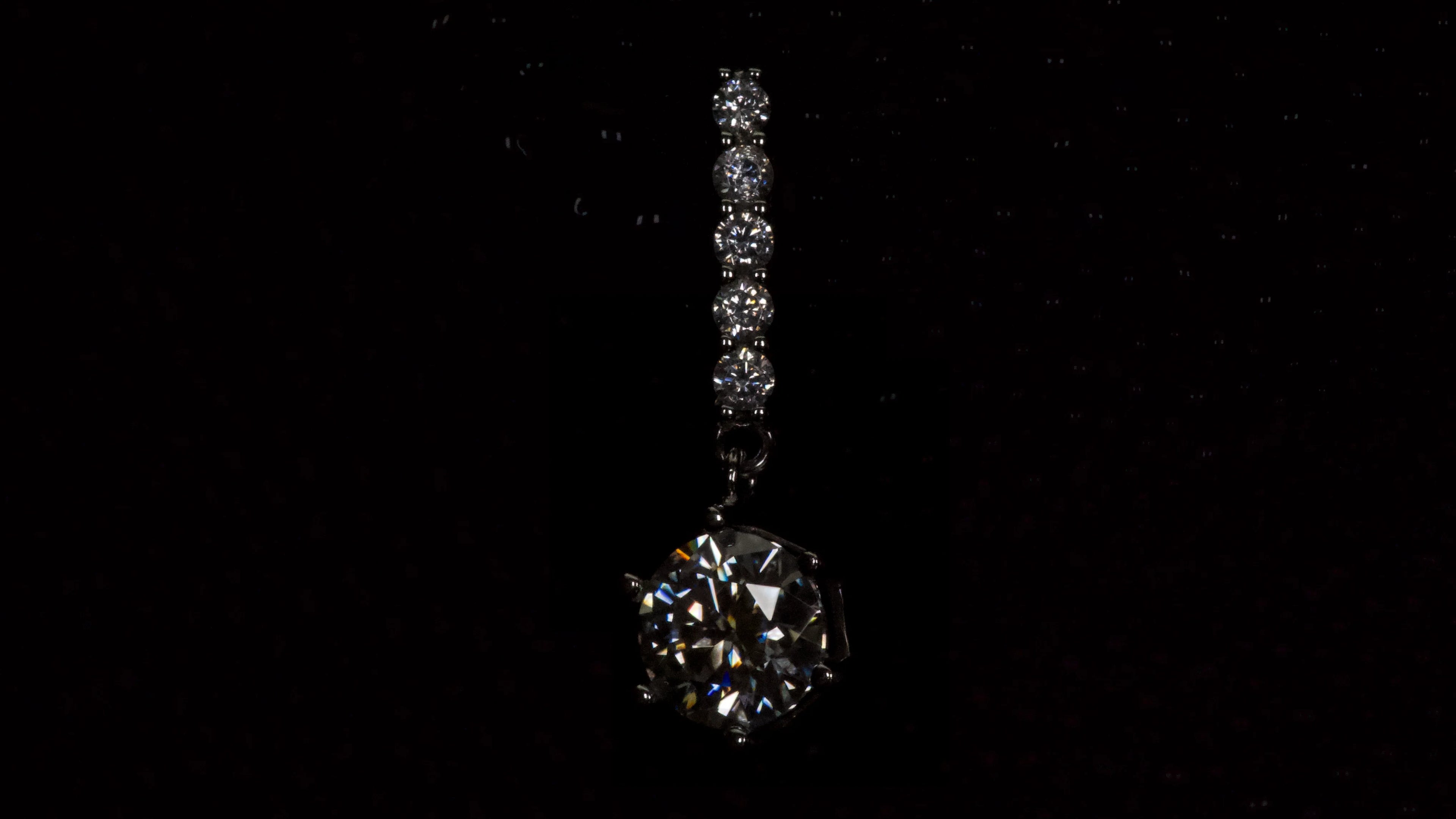Detailwinkel eines Moissanite Ohrrings mit 1ct hängendem Brillantschliff Stein in dunkler Makroaufnahme aus 925 Silber mit Weißgold Veredelung