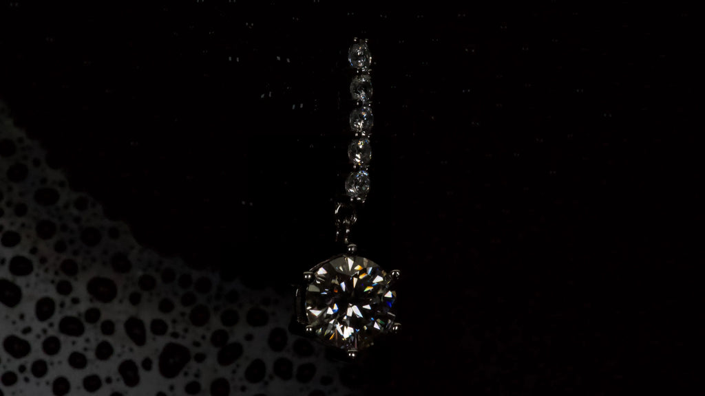 Moissanite Ohrring mit 1ct hängendem Brillantschliff Stein in dunkler Makroaufnahme aus 925 Silber mit Weißgold Veredelung