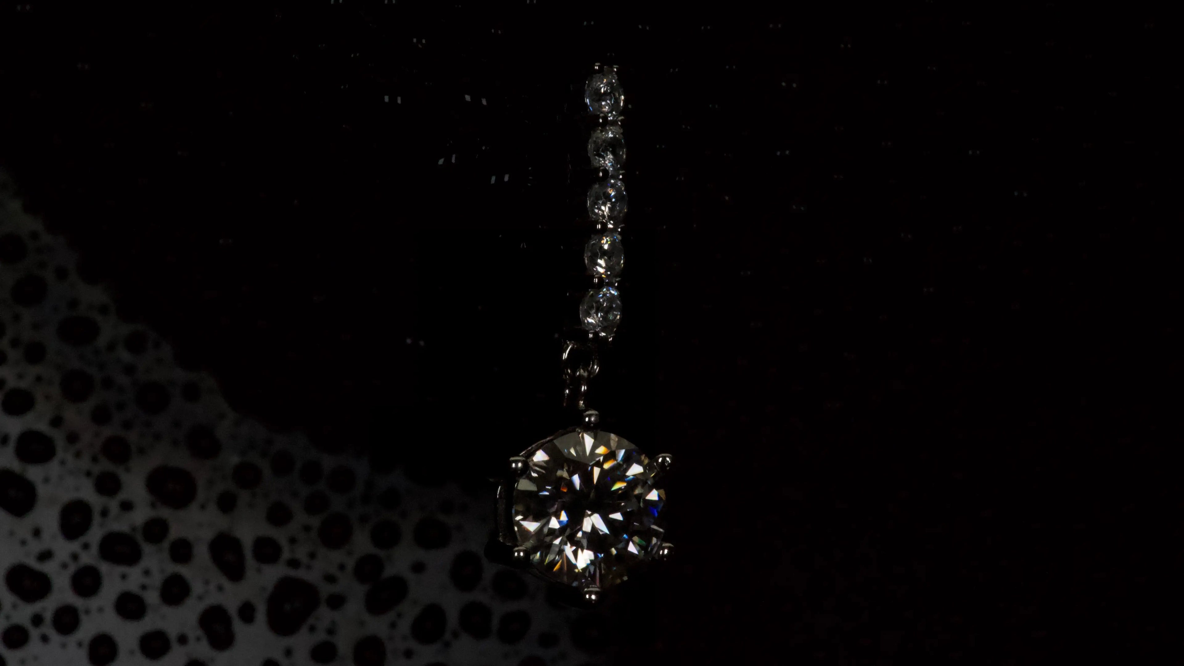 Moissanite Ohrring mit 1ct hängendem Brillantschliff Stein in dunkler Makroaufnahme aus 925 Silber mit Weißgold Veredelung