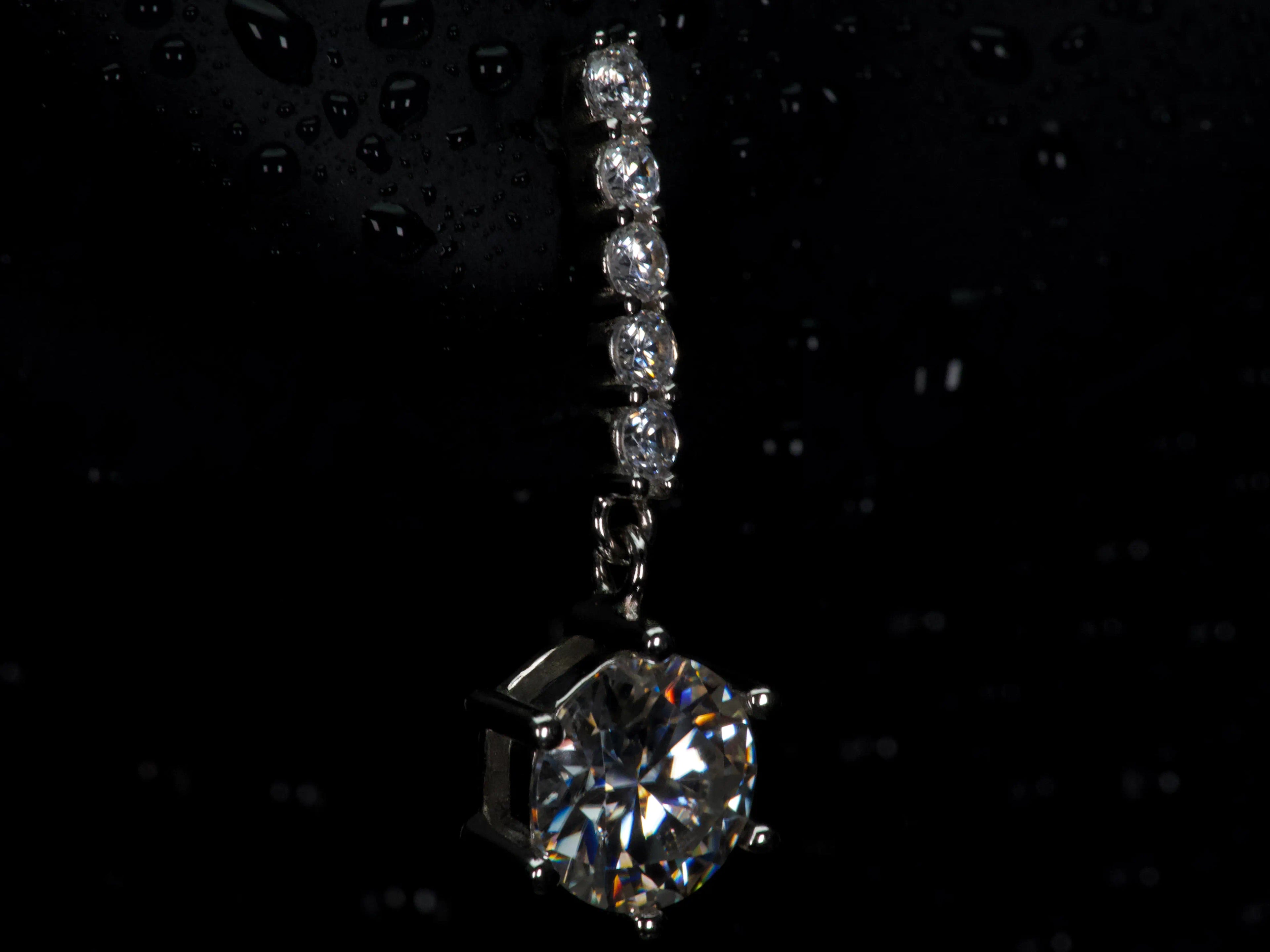 Seitenprofil eines Moissanite Ohrrings mit 1ct hängendem Brillantschliff Stein in dunkler Makroaufnahme aus 925 Silber mit Weißgold Veredelung