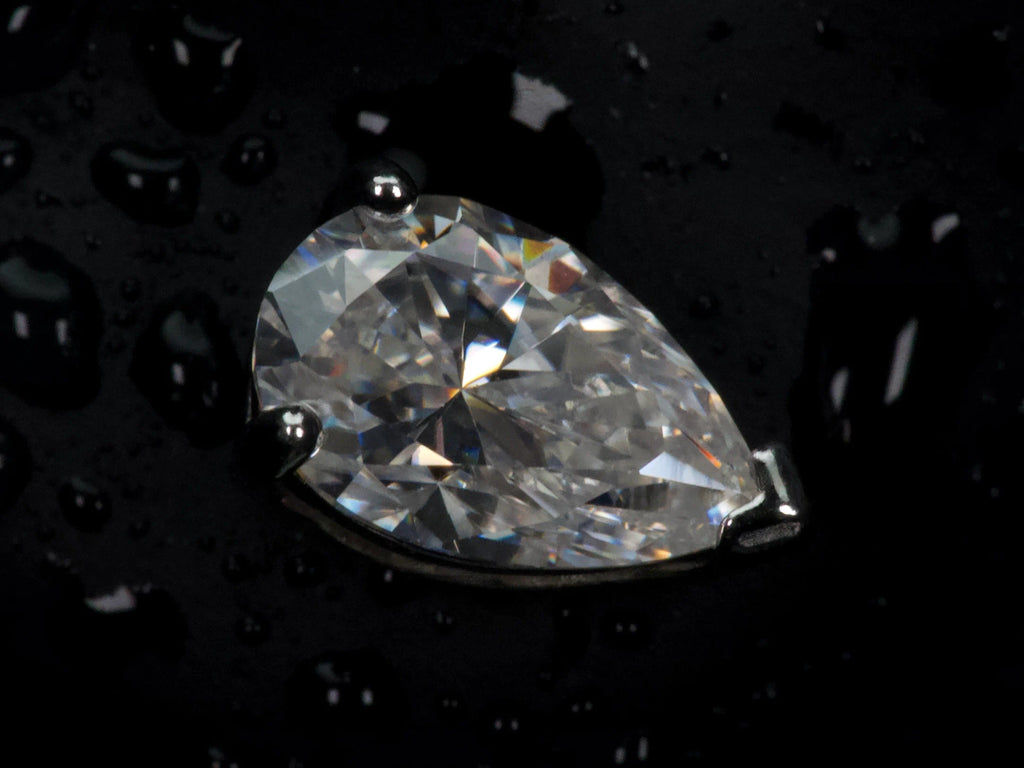 Echte Makroaufnahme eines Moissanite Ohrsteckers im Tropfenschliff – sichtbare Facetten und präziser Pear Cut mit starkem Funkeln und Feuer im Licht, 925 Sterling Silber