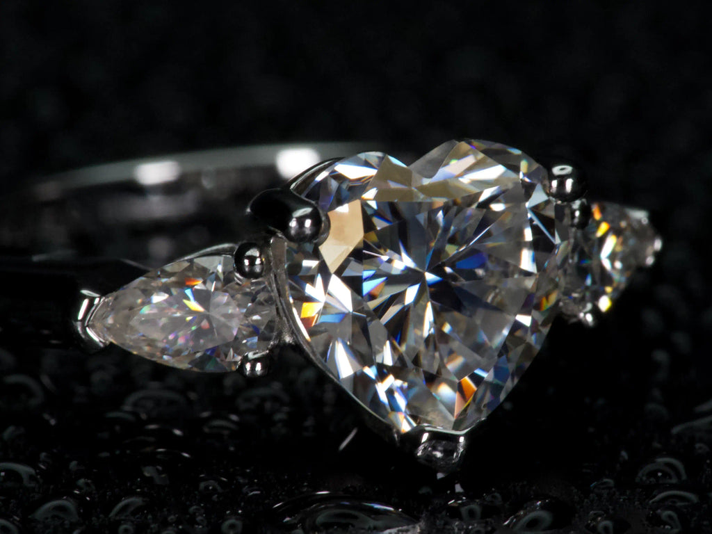 Seitenansicht eines Moissanite Rings mit Herzstein und Tropfen Seitensteinen – offene Fassung für maximalen Lichteinfall und starkes Funkeln ähnlich Diamanten