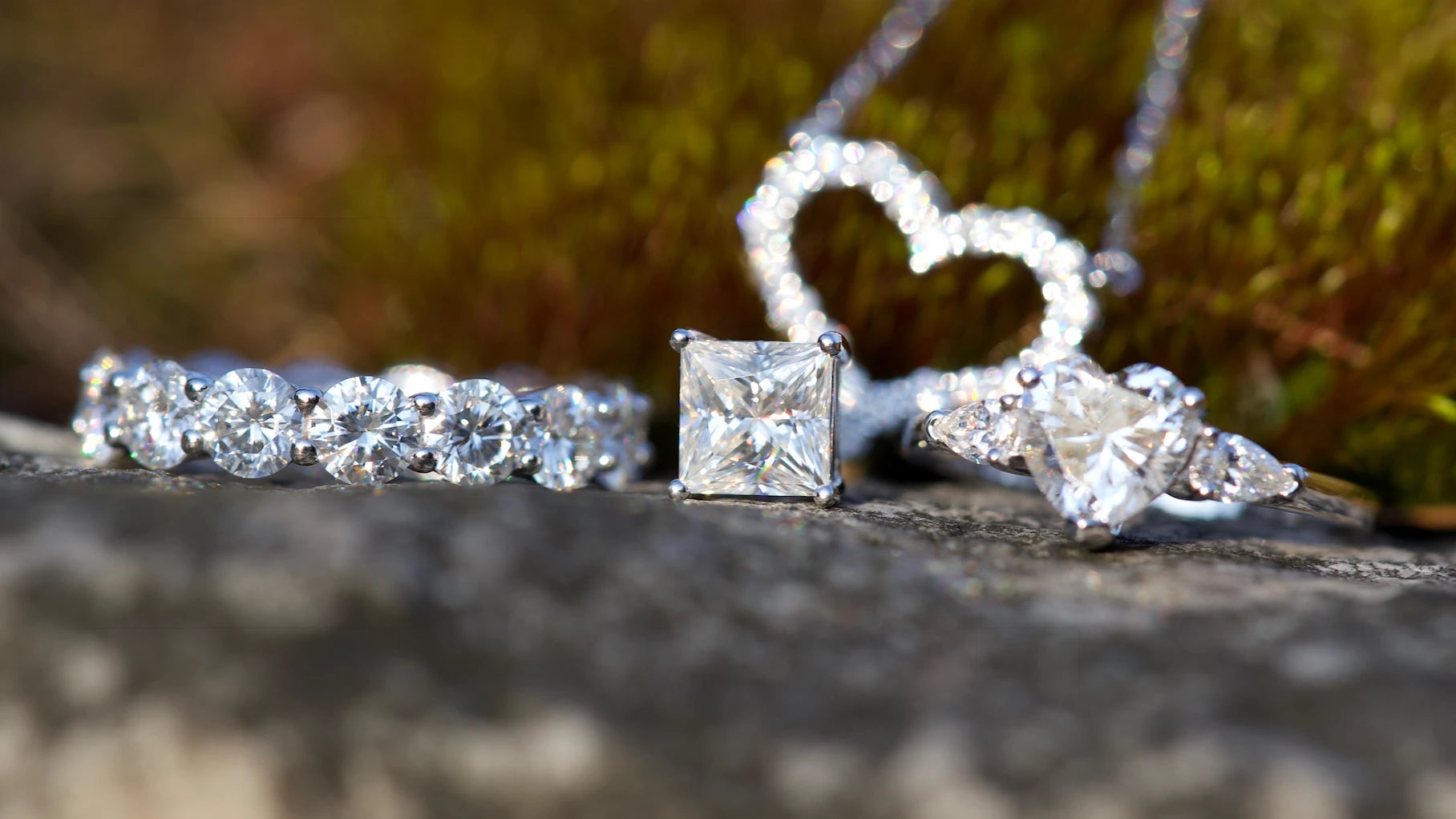 moissanite ringe aus silber mit rundschliff und prinzess schliff neben herz halskette makro schmuckfoto im natürlichen licht auf steinoberfläche