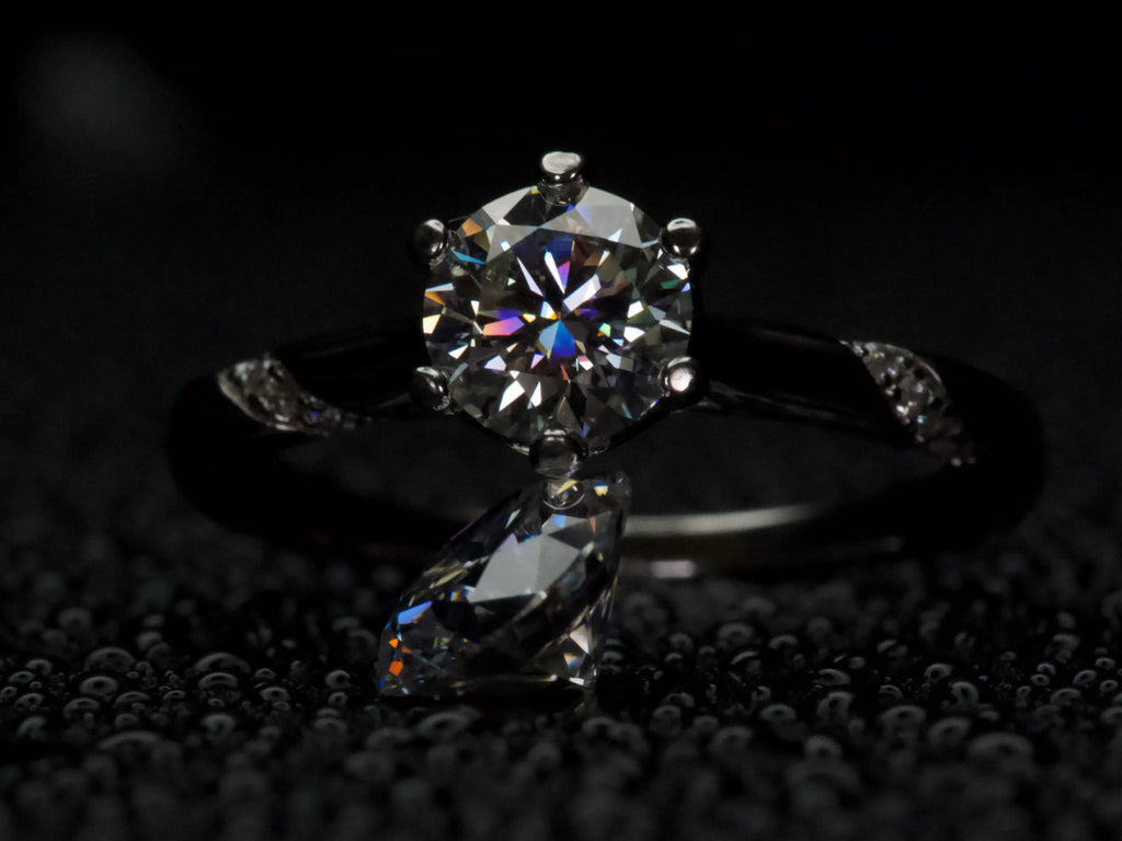 Moissanite Solitär Ring 1ct neben einem 2 ct Moissanite Stein im dunklen Setting, Größenvergleich und intensives Funkeln sichtbar, echte Aufnahme