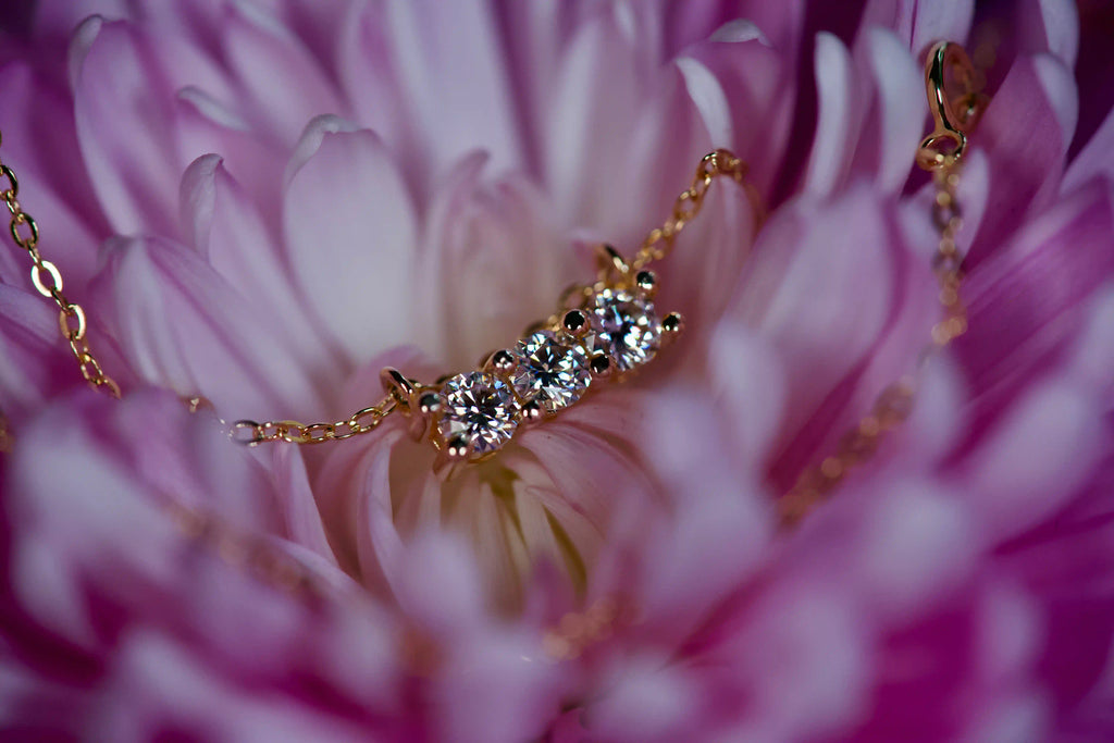 Echte Fotos einer Rose Gold Moissanite Kette mit 3x 3mm Brillant Schliff Steinen in einer Reihe – stärkeres Funkeln als Diamant im echten Licht – extreme Makroaufnahme in rosa Blüte – zeitloses Geschenk mit luxuriösem Feuer und starker Lichtbrechung
